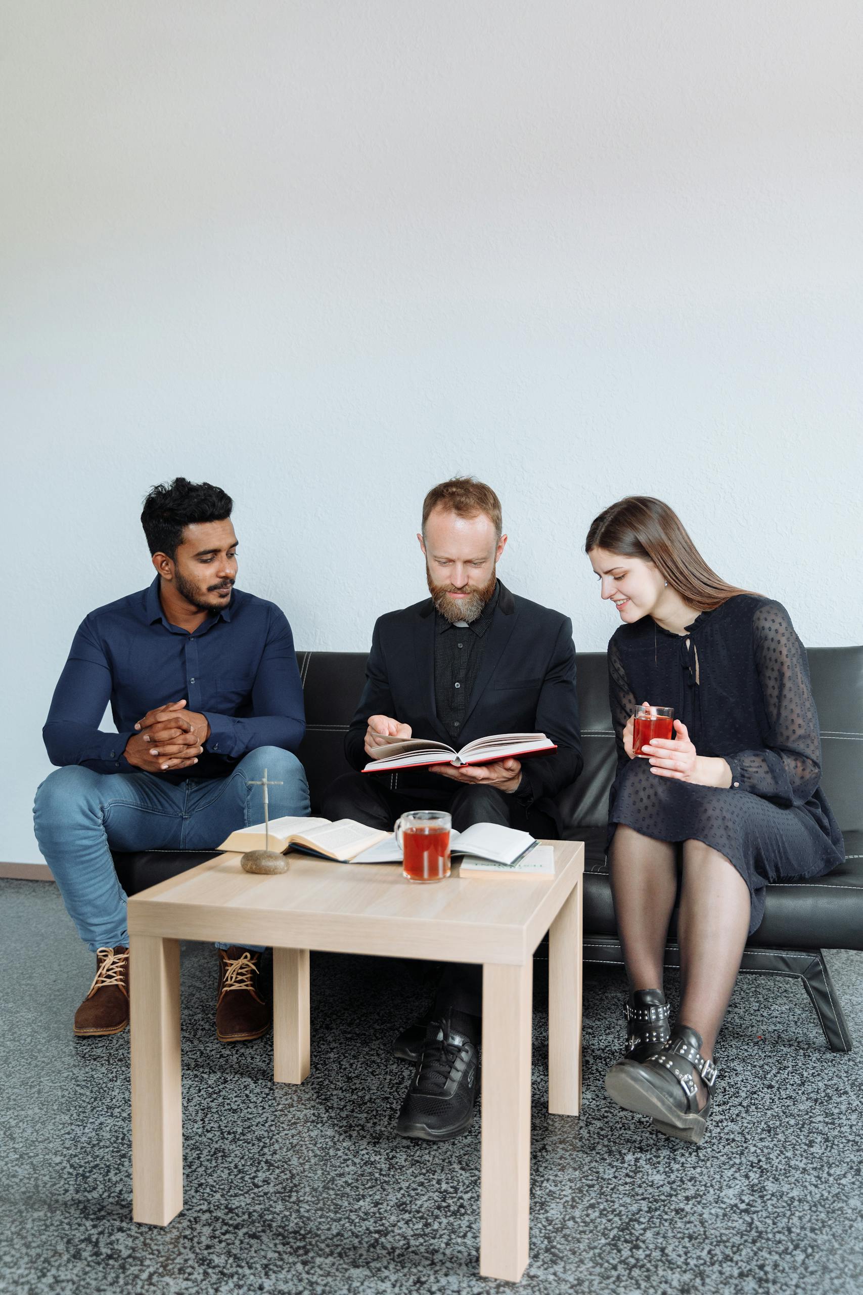 Three adults sitting indoors discussing religious text with open books and drinks.