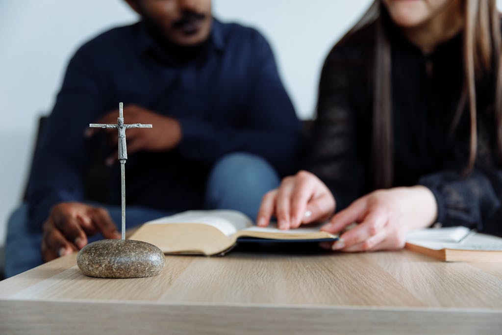 Two individuals study the Bible with a cross on the table, symbolizing faith and devotion.